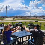 three people clinking their glasses together over a patio table overlooking Willmar Lake