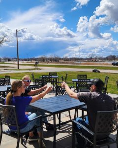 three people clinking their glasses together over a patio table overlooking Willmar Lake